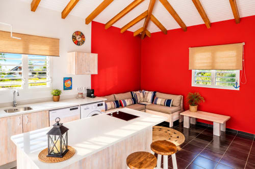L'appartement La cabane du pêcheur au Quetzal à Sainte-Anne : murs rouge vif, cuisine ouverte, canapé beige, vue sur le jardin