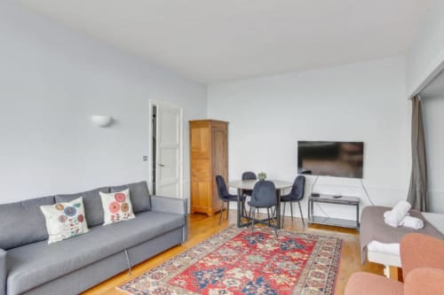 Salon moderne d'appartement parisien avec canapé gris, coin repas, télévision écran plat et armoire en bois à la Résidence Aurmat