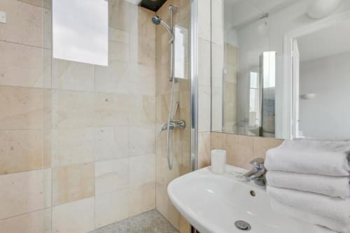 Salle de bain moderne de l'hôtel Paris Boulogne avec carrelage beige, douche vitrée, lavabo blanc et serviettes moelleuses
