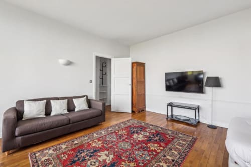Salon contemporain dans un appartement parisien avec canapé marron, télévision écran plat, parquet et tapis aux motifs rouges à la Résidence