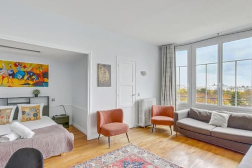 Studio moderne parisien avec lit, fauteuils orange, canapé et vue sur la ville à l'Hôtel Boutique Résidence Aurmat
