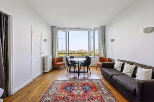 Appartement moderne à la Résidence Aurmat avec canapé, salle à manger et vue sur Paris depuis les baies vitrées