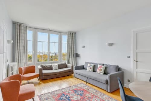 Lumineux salon parisien avec fauteuils orange, canapés gris, grandes fenêtres sur la ville, parquet et