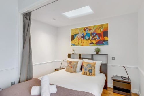 Chambre douillette à la Résidence Aurmat à Paris avec literie blanche, œuvres d'art colorées et équipements modernes