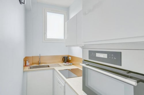 Kitchenette moderne à la Résidence Aurmat Paris avec placards blancs, plan de travail beige, appareils électroménagers inox et fenêtre