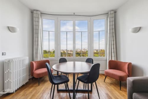 Appartement lumineux et moderne à la Résidence Aurmat Paris avec table à manger ronde, baies vitrées courbes offrant une vue sur la ville, et