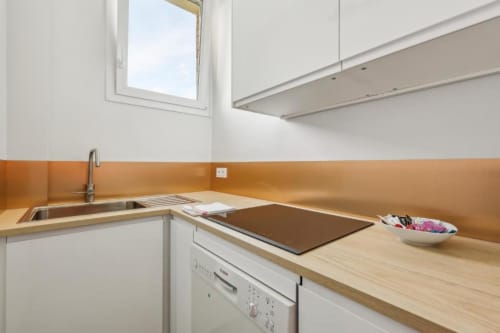 Petite cuisine moderne dans un appartement parisien : plan de travail en bois, évier, cuisinière et dosseret orange