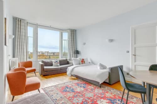 Appartement cosy à la Résidence Aurmat, Paris avec fauteuils orange, canapé gris, lit et vue panoramique sur la ville
