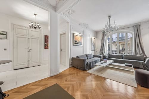 Spacious Trocadéro apartment living room in Paris boutique hotel with herringbone flooring, gray sofa, chandelier, and