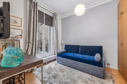 Modern studio apartment at Résidence Aurmat in Paris with blue sofa bed, dining area, and garden view balcony