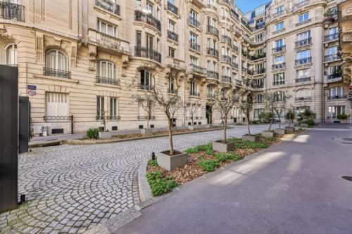 Elegant Parisian courtyard at Résidence Aurmat with classical limestone buildings, manicured trees, and patterned paving