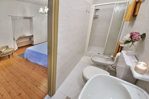 Bagno dell'appartamento La Rosa presso il B&B Roseto del Drago con piastrelle bianche, lavabo, wc, bidet e doccia con porte in vetro.