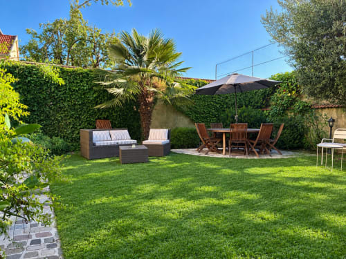Jardin ensoleillé de la maison d'hôtes La Poterne à Épernay avec transats, espace repas, palmier et pelouse verdoyante