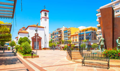 Encantadora plaza de Fuengirola con iglesia blanca, edificios coloridos y esculturas bajo el sol del Mediterráneo