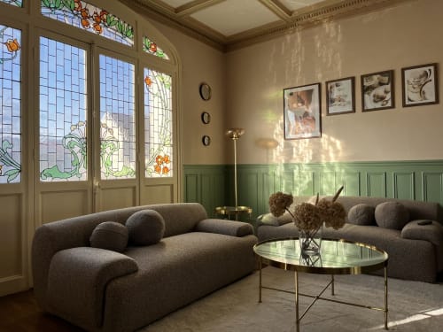 Salon élégant avec canapés gris incurvés, portes vitrées, boiseries vertes et vue sur le jardin du gîte La Poterne