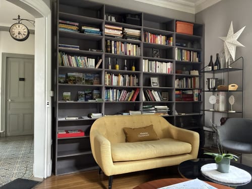 Élégant salon-bibliothèque à La Poterne avec canapé jaune, étagères sombres et livres à Épernay
