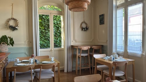 Salle à manger élégante à la Poterne à Épernay avec tables en bois, vue sur le jardin et lampe suspendue tressée