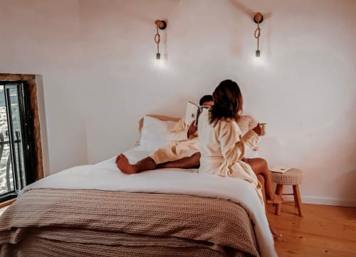 Mulher lendo na cama do hotel Recantos D'Almerinda em Pombal, Portugal, com iluminação aconchegante e piso de madeira.
