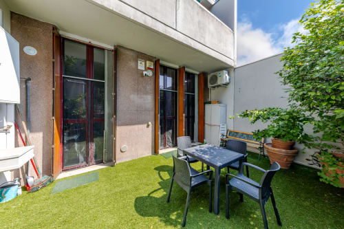 Terrazza giardino privato di RenTIAMOMilano con tavolo da pranzo esterno, sedie, prato sintetico e pareti di edera verde a Milano