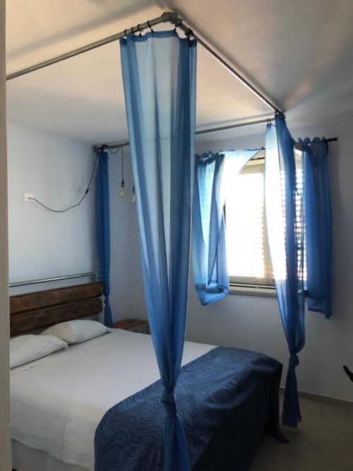 Letto a quattro colonne blu con tende in velo in una camera luminosa dell'Agriturismo il Mandriolo, Marina di Grosseto