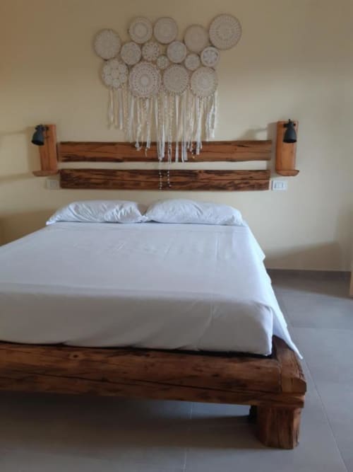 Letto rustico in legno con biancheria bianca e macramé sopra la testata in una camera da letto rustica italiana con vista sul giardino