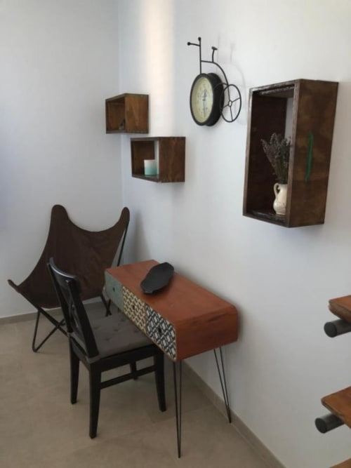 Moderna zona living con poltrona nera, pouf in terracotta, scaffali in legno a parete, orologio bicicletta vintage e
