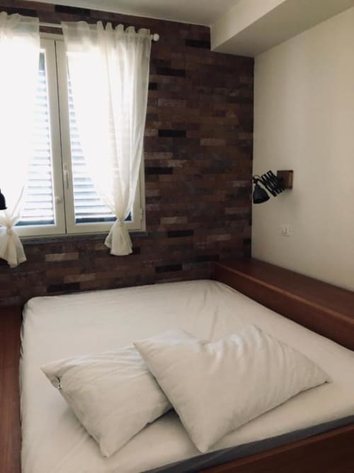 Camera da letto matrimoniale accogliente con cuscini bianchi, parete in legno scuro, finestra con tende color crema e vista sul giardino