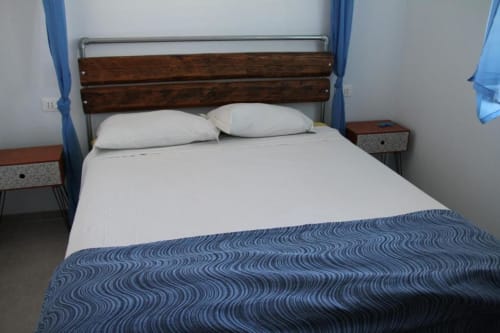 Camera da letto con letto in legno, biancheria bianca, due cuscini, plaid blu a motivi e comodini presso Agriturismo il