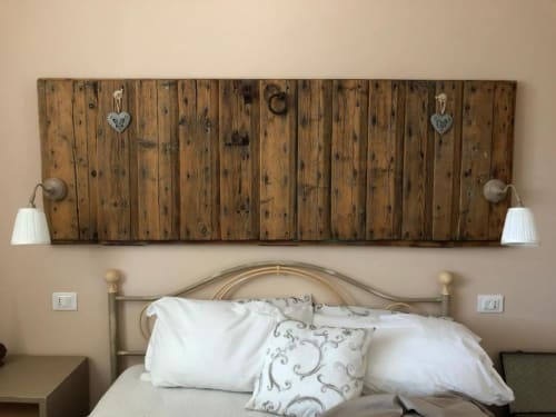 Testata rustica in legno con cuscini bianchi e dettagli decorativi a forma di cuore sopra il letto dell'agriturismo il Mandriolo.