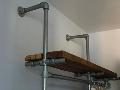 Appendiabiti industrial in tubo metallico con ripiano in legno montato su parete bianca in appartamento