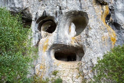 Rosto de pedra envelhecida com traços ocos cobertos de musgo e líquen perto de Pombal, Portugal
