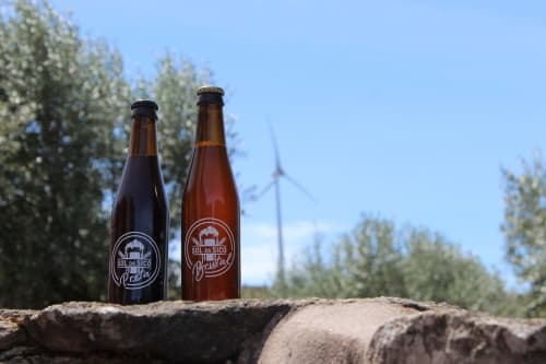 Duas garrafas de cerveja Sol da Sicilia em um tronco com floresta e turbina eólica em Recantos d'Almerinda, Pombal