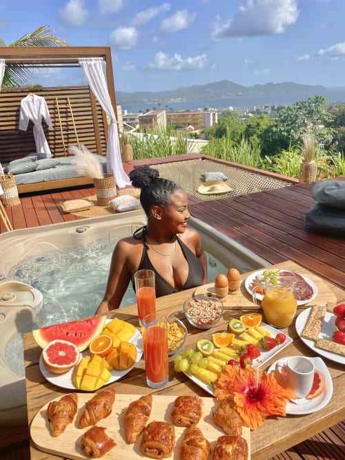 Femme savourant son petit-déjeuner dans le bain à remous des Suites et Spa Creole Bay à Fort-de-France avec vue sur la baie