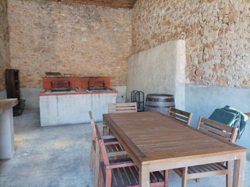 Rustic dining area at Domaine Le Piboul with wooden table, brick walls, and outdoor kitchen in Fontcouverte