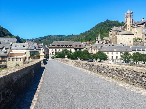 Pont en pierre médiéval et bâtiments du village d'Estaing, région du Lot, France avec rivière et collines boisées
