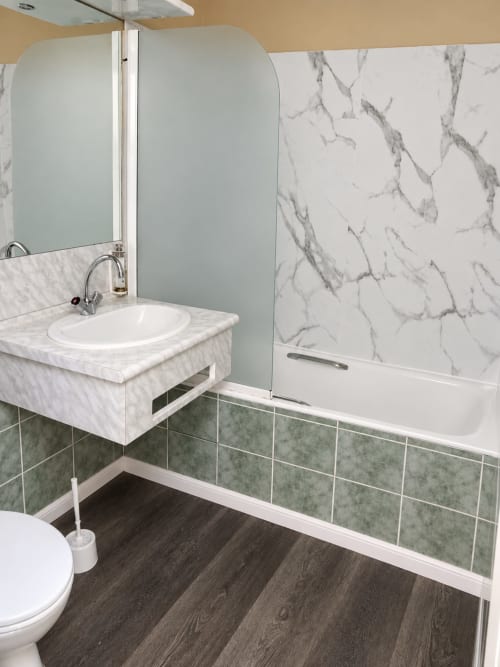 Salle de bains contemporaine avec lavabo en marbre, baignoire blanche, accents de carrelage vert et parquet foncé à l'Hôtel du pont d'Estaing