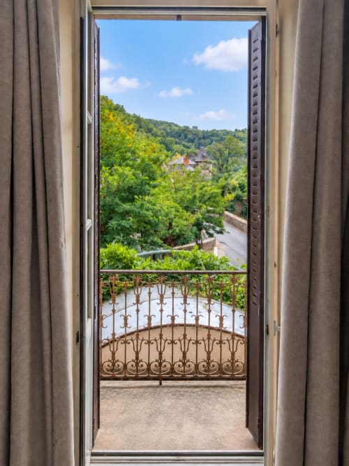 Balcon orné de l'Hôtel du pont d'Estaing surplombant le village, verdure luxuriante et rivière