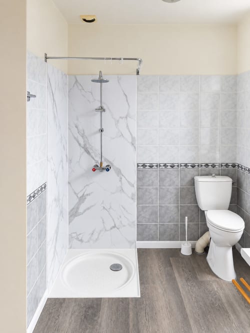 Salle de bain moderne avec douche en marbre, toilettes blanches et sol imitation bois à l'Hôtel du pont d'Estaing