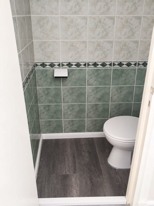 Salle de bain moderne avec carrelage en marbre, carreaux d'accent verts, toilettes blanches et sol imitation bois foncé à l'Hôtel du Pont