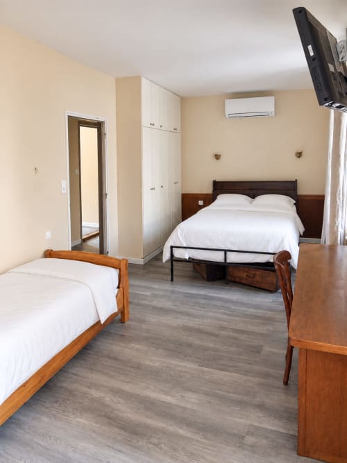 Chambre de l'Hôtel du Pont d'Estaing avec deux lits en bois, draps blancs, murs beige et climatisation