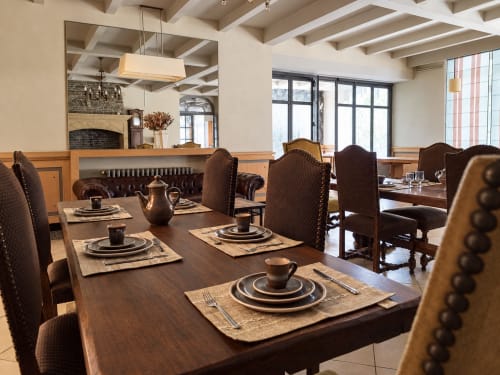 Élégante salle à manger de l'Hôtel du pont d'Estaing avec tables en bois, chaises bordeaux, cheminée et grandes fenêtres à Estaing