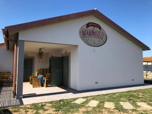 Ingresso dell'Agriturismo il Mandriolo, rustica casa colonica bianca con persiane verdi e insegna in Italia