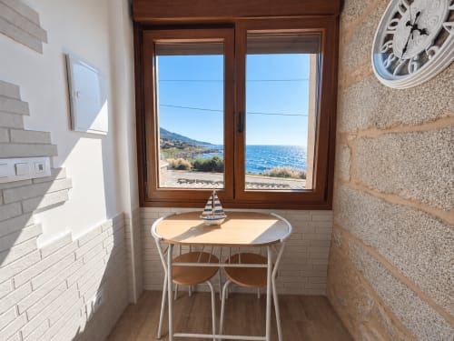 Rincón comedor de cabaña costera con vistas al mar en Holibai, As Mariñas, mesa de madera y océano visible a través de puertas de cristal