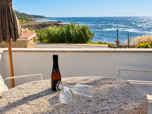 Botella de cerveza y vasos en la mesa de la terraza costera de la casa Holibai en As Mariñas, España, con vistas al mar azul