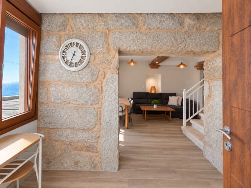 Sala de estar de casa de piedra con vistas al mar, vigas de madera, reloj, sofá negro y comodidades modernas en el hotel Holibai