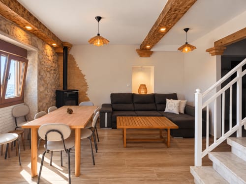 Sala de estar moderna en Holibai, As Mariñas con vigas de madera, estufa negra, mesa de comedor, sofá oscuro y escaleras