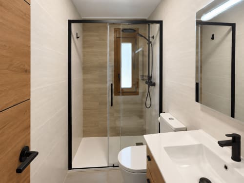 Baño moderno en casita Holibai con mampara de ducha de marco negro, tocador blanco y acabados de azulejos neutros