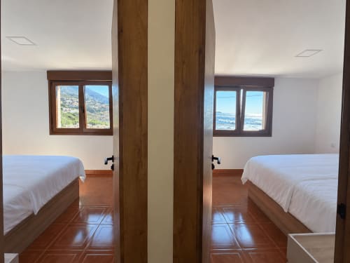 Vista espejo de camas gemelas en la cabaña As Mariñas con vistas al mar a través de ventanas y suelo de terracota