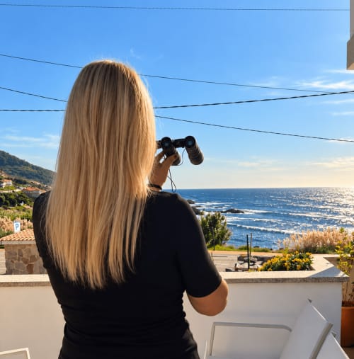 Mujer con binoculares observando el mar desde el balcón de una casita en Holibai, As Mariñas