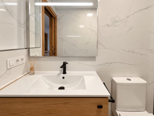 Baño moderno en la casa rural Holibai con baldosas de mármol, lavamanos blanco, grifo negro, espejo e inodoro en As Mariñas